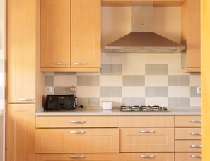 A kitchen with wooden cabinets, a gas stove, a toaster, and a tiled backsplash. - Horizon Retreat, Sea View A12 (Óbidos)