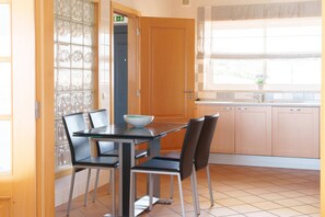 A dining area with a table and chairs, a kitchen with cabinets and a window, and a door leading to another room. - Horizon Retreat, Sea View A12 (Óbidos)