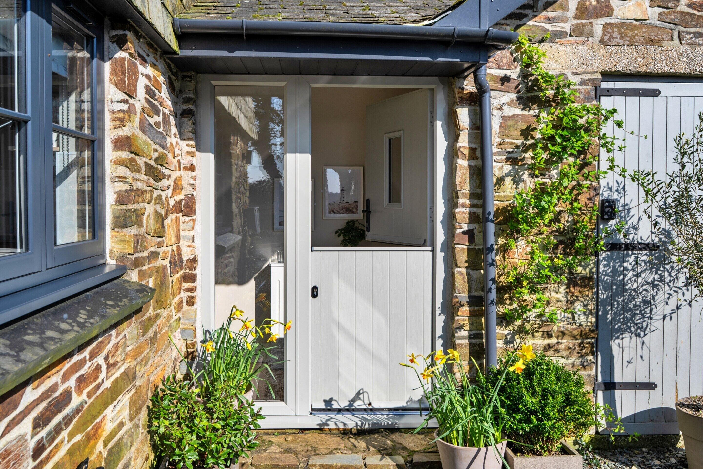 A stone house with a white door, a window, and a small garden with yellow flowers.