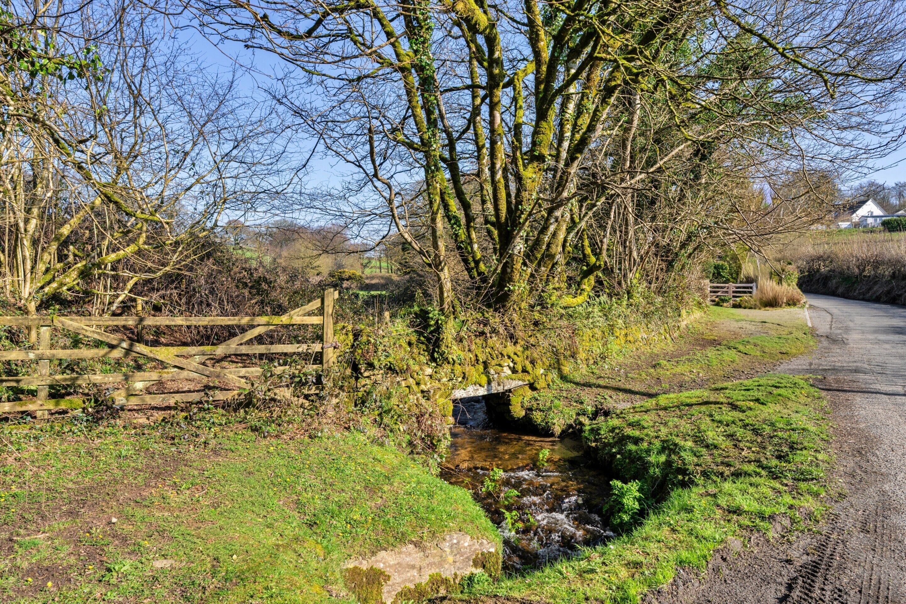 A rural landscape with a narrow stream, a wooden fence, and a stone bridge.