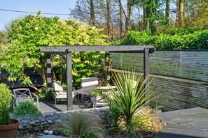 Un patio jardín con pérgola, zona de estar y diferentes plantas.