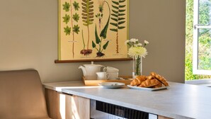 Eine Küchenzeile mit Esstisch, einem weißen Teekessel, Tassen und einem Teller mit Croissants.
