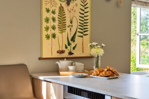 A kitchen area with a dining table, a white teapot, cups, and a plate of croissants. - Luxury Lodge With Hot Tub (Camelford)