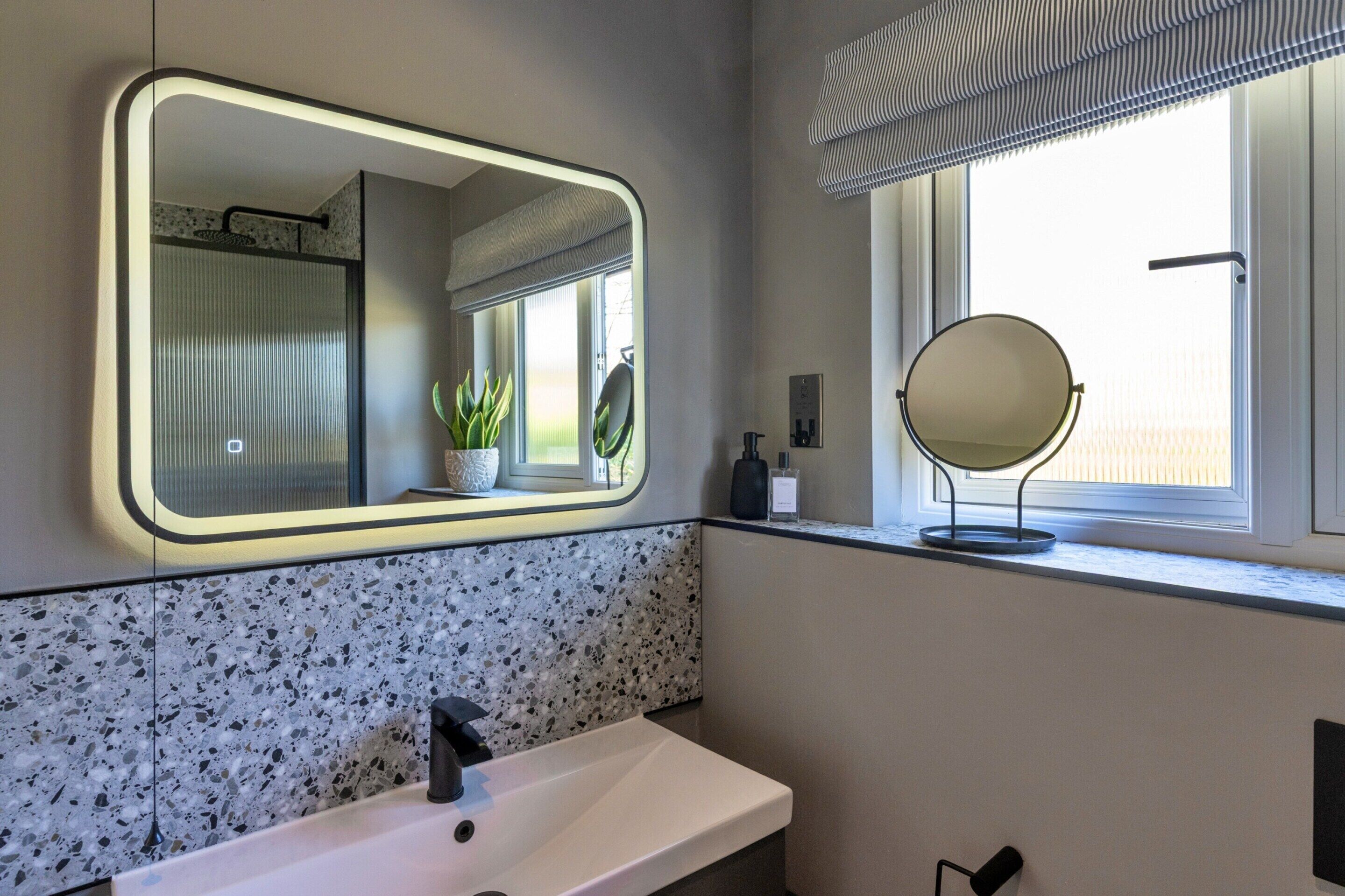 A bathroom with a white sink, a mirror, and a window with a view of the outside.