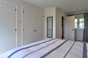 Une chambre à coucher avec un lit, deux armoires blanches, un miroir et une fenêtre avec des rideaux.