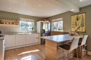 A modern kitchen with a central island, white cabinetry, and a large window providing natural light. - Luxury Lodge With Hot Tub (Camelford)