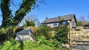 Ein Steinschild mit der Aufschrift 'Thyme Bank', ein hölzernes Tor und ein Steinhaus mit grauem Dach.