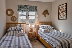 A bedroom with two single beds, a window with a view, and a wall-mounted mirror. - Luxury Lodge With Hot Tub (Camelford)