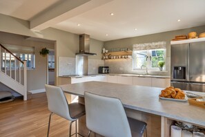 A modern kitchen with a central island, stainless steel appliances, and a dining area with two chairs. - Luxury Lodge With Hot Tub (Camelford)