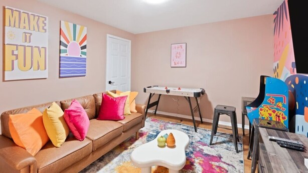 A cozy living room with a brown leather couch, colorful pillows, a white coffee table, a foosball table, and a vibrant chair. - Lake Front! Hot Tub, Fire Pits, Game Room (East Stroudsburg)