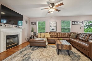 A living room with a fireplace, leather sofa, coffee table, and a ceiling fan. - Lake Front! Hot Tub, Fire Pits, Game Room (East Stroudsburg)