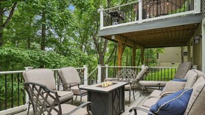 A covered deck with outdoor furniture, a fire pit, and a view of the surrounding greenery. - Lake Front! Hot Tub, Fire Pits, Game Room (East Stroudsburg)
