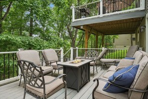 A covered deck with outdoor furniture, a fire pit, and a view of the surrounding greenery. - Lake Front! Hot Tub, Fire Pits, Game Room (East Stroudsburg)