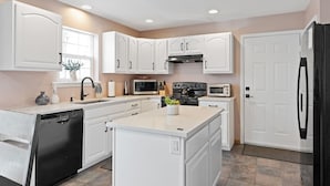 A modern kitchen with white cabinetry, a central island, a dishwasher, a stove, a microwave, and a refrigerator. - Lake Front! Hot Tub, Fire Pits, Game Room (East Stroudsburg)