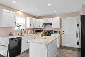 A modern kitchen with white cabinetry, a central island, a dishwasher, a stove, a microwave, and a refrigerator. - Lake Front! Hot Tub, Fire Pits, Game Room (East Stroudsburg)
