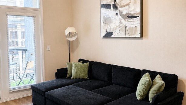 Een moderne woonkamer met een modulaire bank, een vloerlamp en een groot abstract schilderij aan de muur.