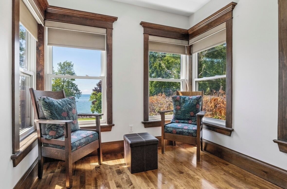 A corner room with two chairs facing a bay window overlooking a body of water.