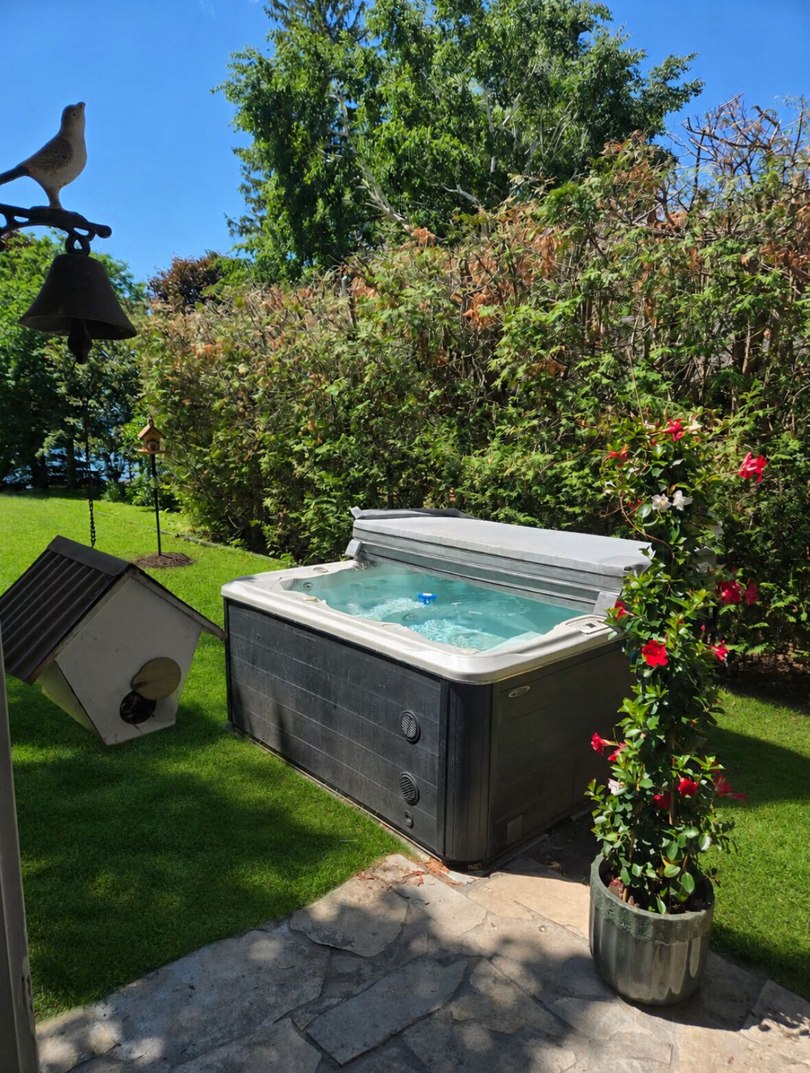 A hot tub in a garden with a birdhouse and a bird feeder.