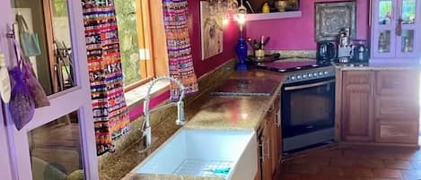 Una cocina con encimeras de granito, armarios de madera, una estufa y una pata para colgar ollas.