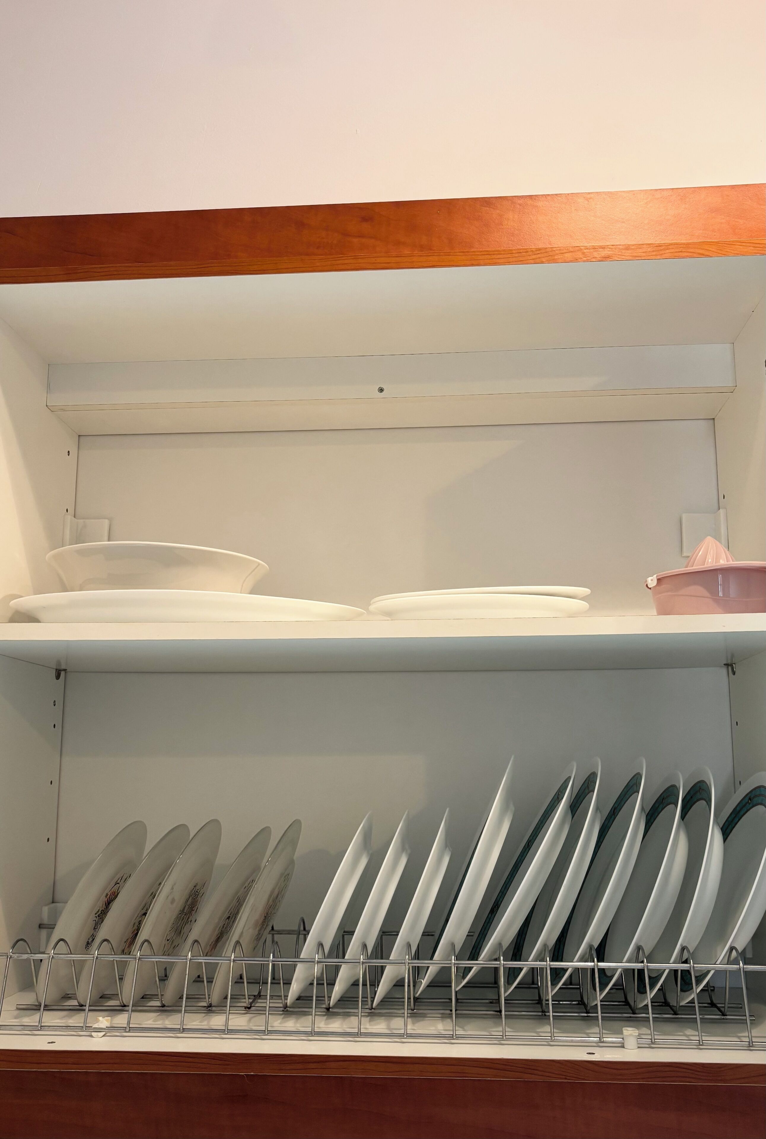 En køkkenhylde med hvide tallerkener, skåle og en opvaskestativ med tallerkener.
