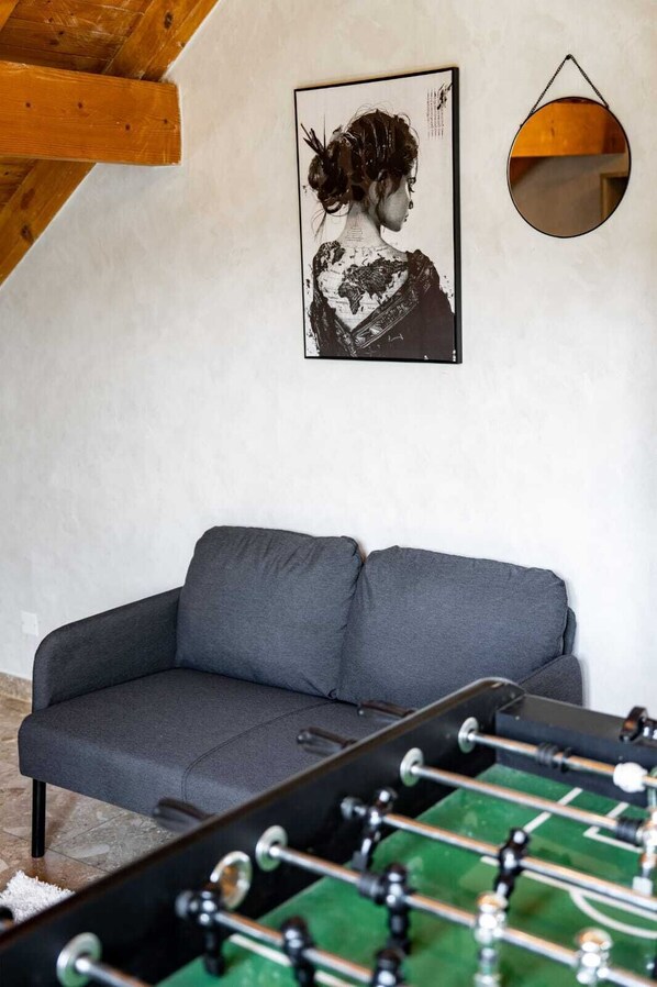 Una habitación con un sofá gris, una obra de arte enmarcada en la pared y una mesa de fútbol.