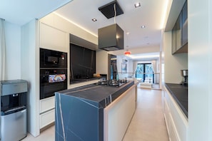 A modern kitchen with integrated appliances, a central island, and a view to the living area. - Luxury Renovated New Villa in the heart of Kalkan (ANTALYA)