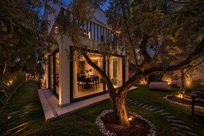 Una casa moderna con un porche acristalado, comedor y jardín bien cuidado con un árbol y un sendero de piedra.