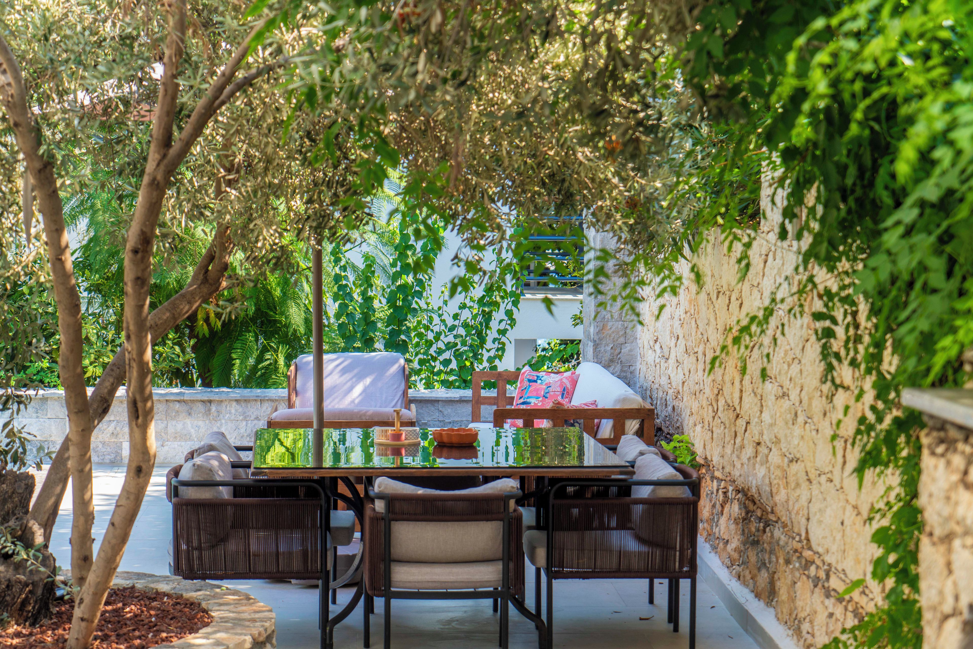 An outdoor seating area with a table and chairs, surrounded by greenery and a stone wall.
