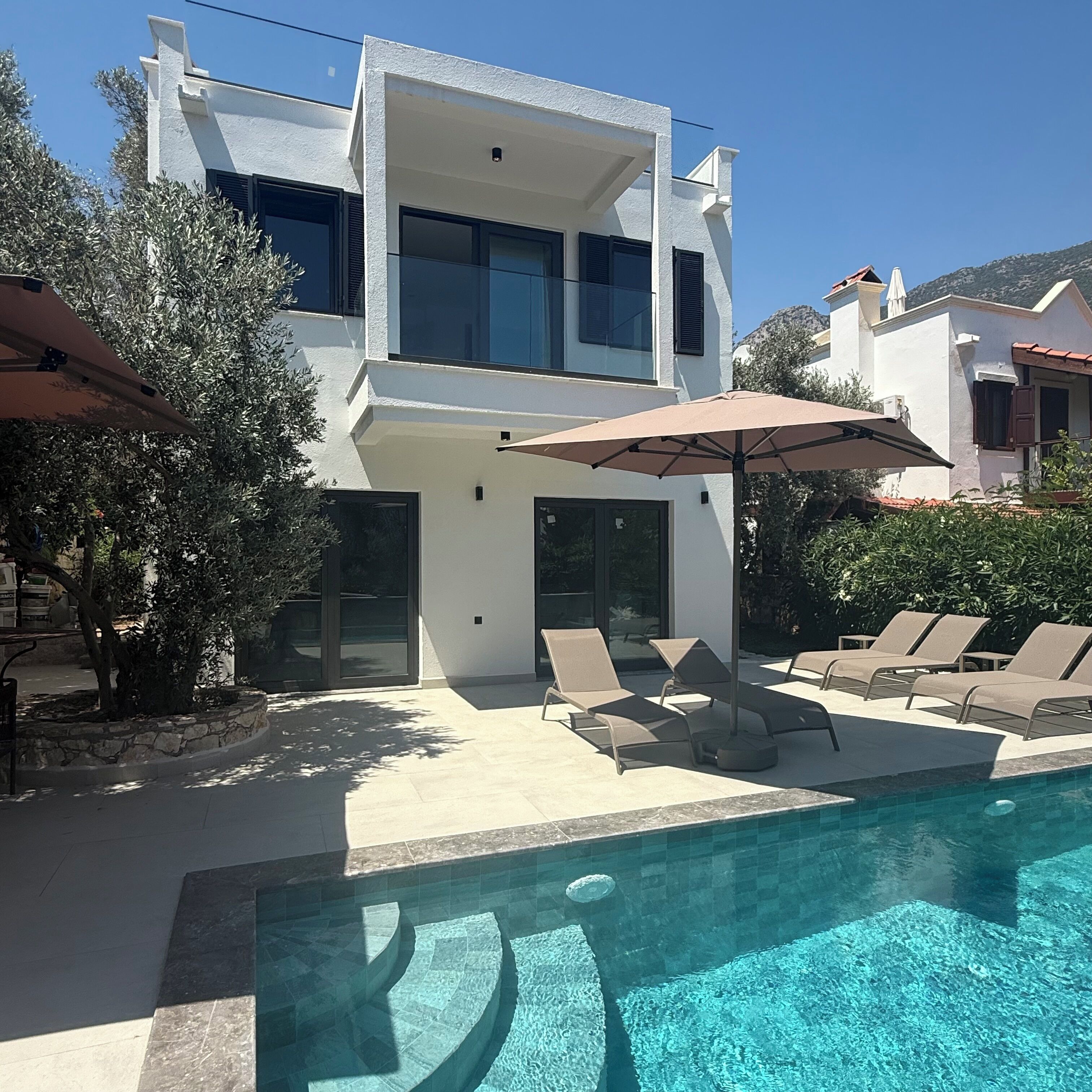 A modern two-story building with a swimming pool, outdoor seating, and a clear sky.