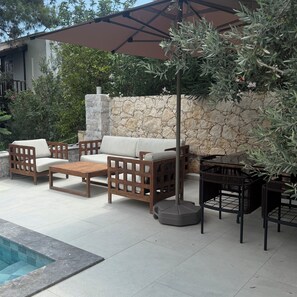Ein Außenbereich mit Sitzgelegenheit, einer Steinmauer, einem Pool und einer Pergola.
