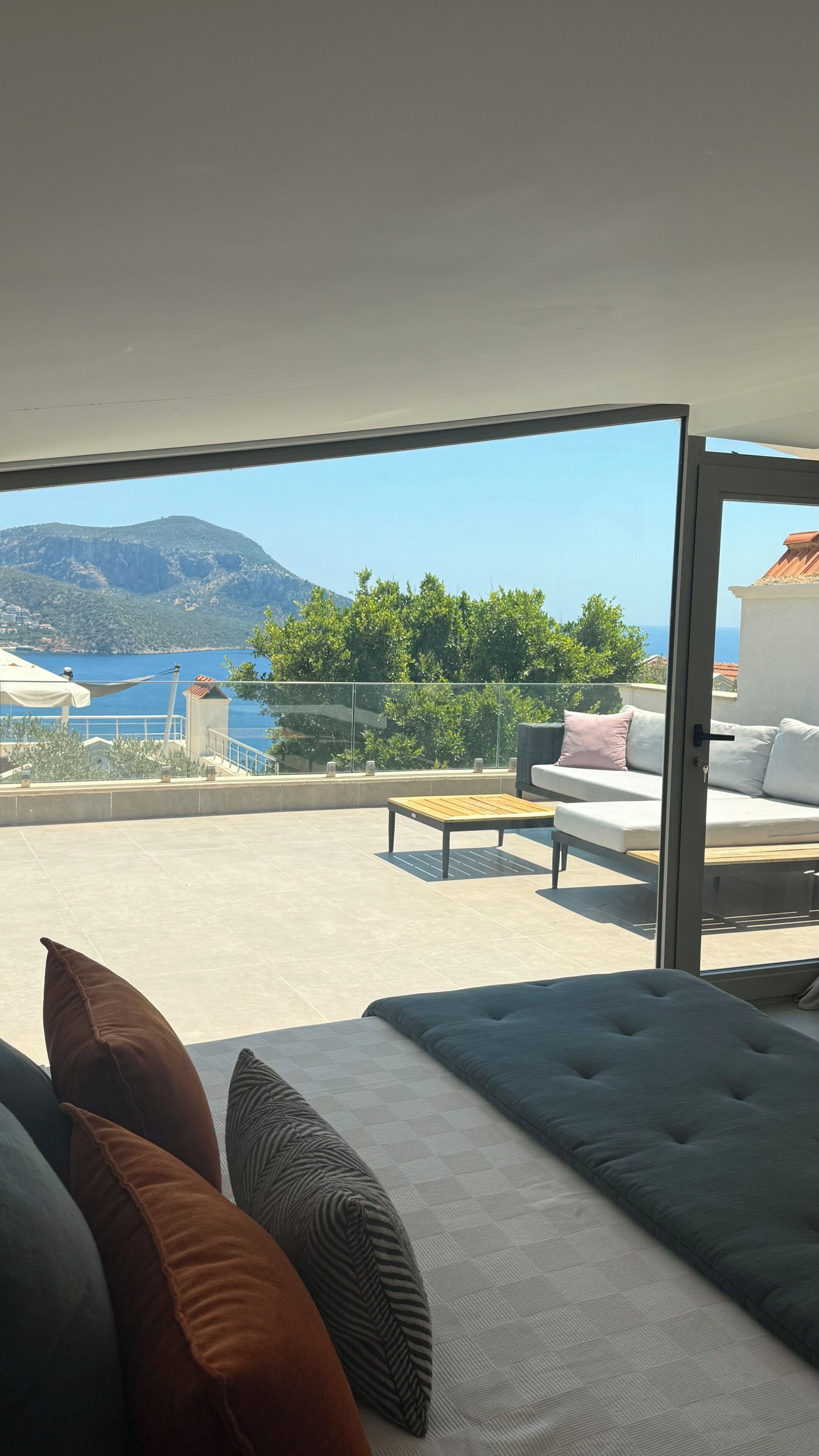 A balcony with a view of the sea and mountains, a sofa, and a table.