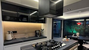 A modern kitchen with a central island, black cabinetry, and a built-in stove. - Luxury Renovated New Villa in the heart of Kalkan (ANTALYA)