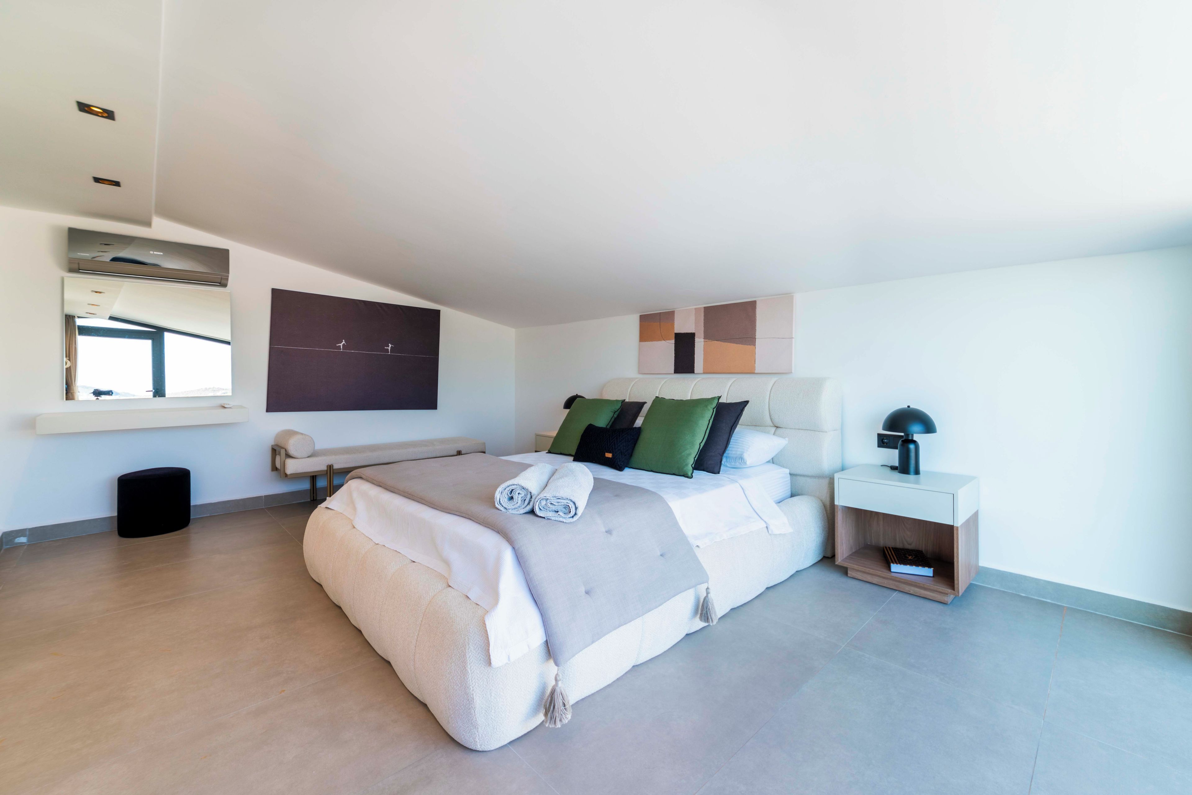 A modern bedroom with a large bed, a bedside table, a nightstand, a window, and a wall-mounted artwork.