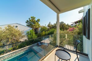 A balcony with a glass railing overlooking a swimming pool and a garden. - Luxury Renovated New Villa in the heart of Kalkan (ANTALYA)