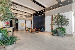 A modern lobby with a reception desk, seating area, and potted plants.