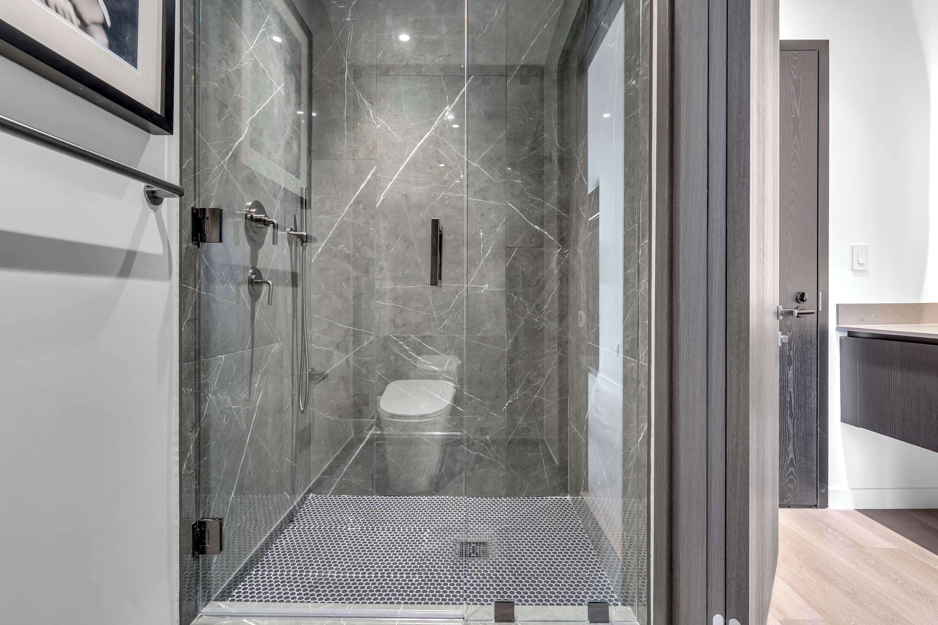 Une salle de bain moderne dotée d’une douche à parois de verre, de toilettes et d’un espace lavabo.