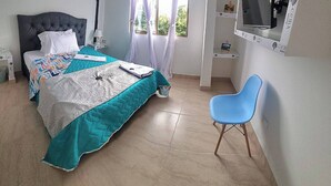 Una camera da letto con un letto, una sedia, una TV e una finestra con tende.