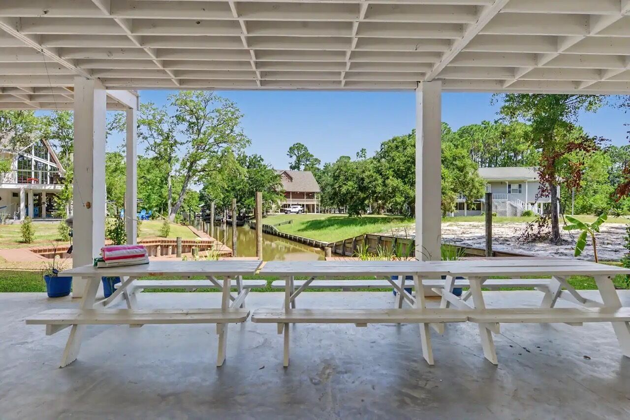 An outdoor covered area with picnic tables, a view of a residential area, and a small body of water.
