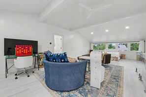 A spacious room with a large window, a ceiling fan, a round seating area, and a desk with a computer monitor. - Brand New Beautiful House on the Water in Timber Ridge (Pass Christian)