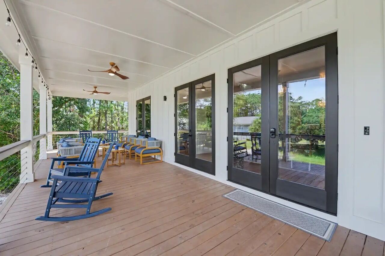 Un espace extérieur abrité, doté d’un plancher en bois, d’un mobilier de jardin et de portes vitrées donnant sur un jardin.