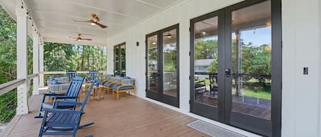 Un espace extérieur abrité, doté d’un plancher en bois, d’un mobilier de jardin et de portes vitrées donnant sur un jardin.