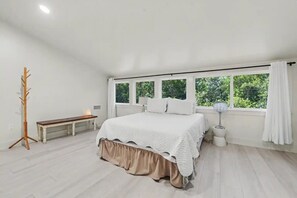 Un dormitorio con una cama grande, un banco, una mesita de noche y una ventana con cortinas.