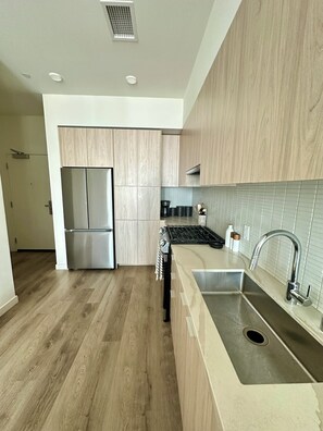A modern kitchen with wooden cabinets, stainless steel appliances, and a tiled backsplash. - Cozy 1-bedroom apartment with Luxury Amenities in Downtown San Diego (San Diego)