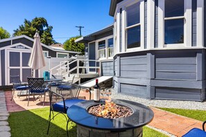 Ein Garten mit Feuerstelle, Gartenmöbeln und einer überdachten Terrasse.
