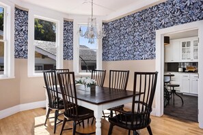 Uma sala de jantar com uma mesa de madeira escura, seis cadeiras pretas e um lustre.