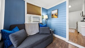 A room with a grey sofa, blue walls, a window with blinds, a lamp, and a painting. - Chestnut Cottage- Cozy Cottage for Two! (Paso Robles)