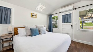 A bedroom with a bed, a nightstand, a lamp, a picture on the wall, and a window with curtains. - Chestnut Cottage- Cozy Cottage for Two! (Paso Robles)