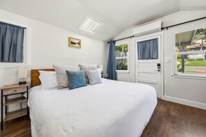 A bedroom with a bed, a nightstand, a lamp, a picture on the wall, and a window with curtains. - Chestnut Cottage- Cozy Cottage for Two! (Paso Robles)