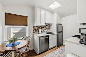 A modern kitchen with white cabinetry, a stainless steel refrigerator, and a coffee machine. - Chestnut Cottage- Cozy Cottage for Two! (Paso Robles)