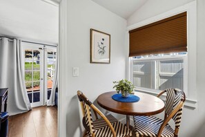 Ein Zimmer mit einem runden Holztisch, zwei gewobenen Stühlen, einem Blumentopf und einer gerahmten Pflanzenillustration an der Wand.